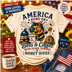 Woman wearing a cream-colored patriotic farmhouse t-shirt featuring a colorful bee in American flag sunglasses holding a coffee mug that reads "Caffeine First." The back design includes beehives, honey dippers, fireworks, stars, and patriotic red, white, and blue accents with the phrase "America Runs on Bees & Coffee with Stars, Stripes & Honey Hives." The woman is standing on a rustic farmhouse porch decorated with American flags, sunflowers, lanterns, and a "God Bless America" coffee mug.